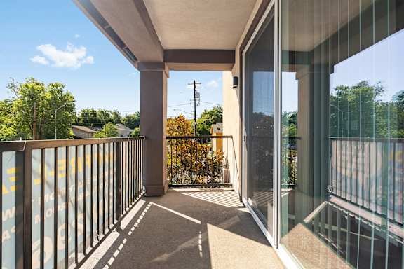 Balcony off of the living room. Concrete floor with vertical metal railing along balcony. Sliding glass door that opens up to the living room with a screen door and vertical blinds.