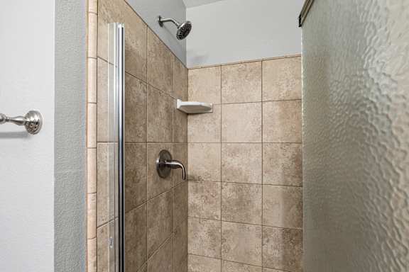Walk-in shower with beige tile and glass door at OSM Properties Homes & Apartments, Chico