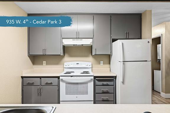 A kitchen with a white stove and refrigerator, and grey cabinets.
