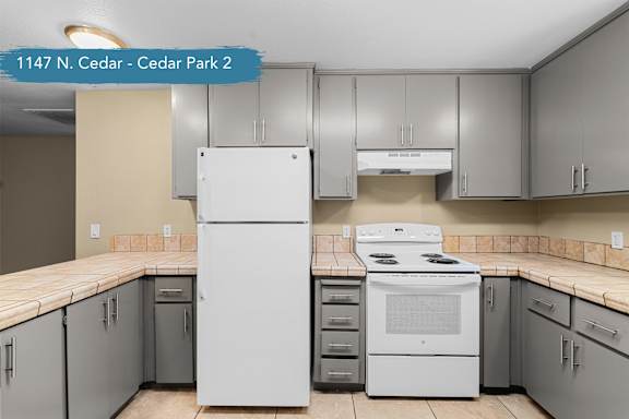 A kitchen with a white fridge and stove, and grey cabinets.