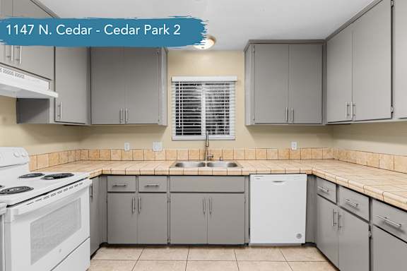A kitchen with a white stove and grey cabinets.