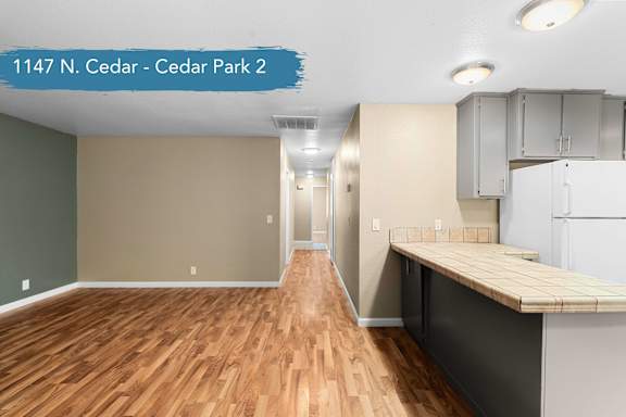 A room with wood flooring and a kitchen area with a counter and cabinets.