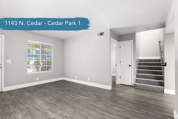 A spacious room with wooden flooring and a staircase leading to another room.