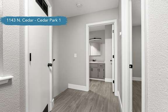 A hallway with a door on the left and a kitchen area visible through the door.