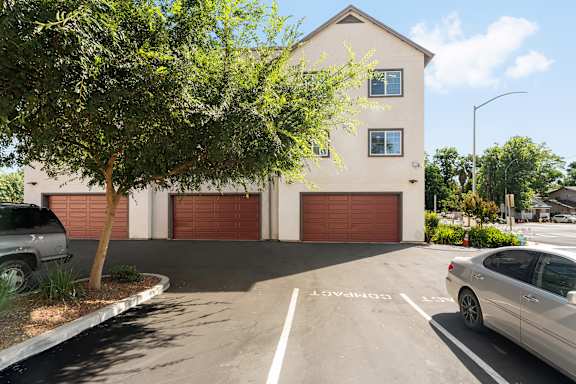 Exterior of building showing two story townhomes with garage doors facing parking lot with trees.