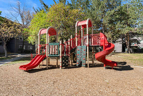 A playground with a red slide and a green and red climbing structure.
