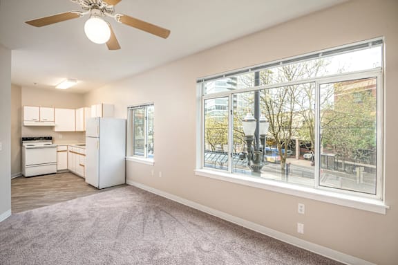 A spacious living room with a ceiling fan and a kitchen area with white appliances.