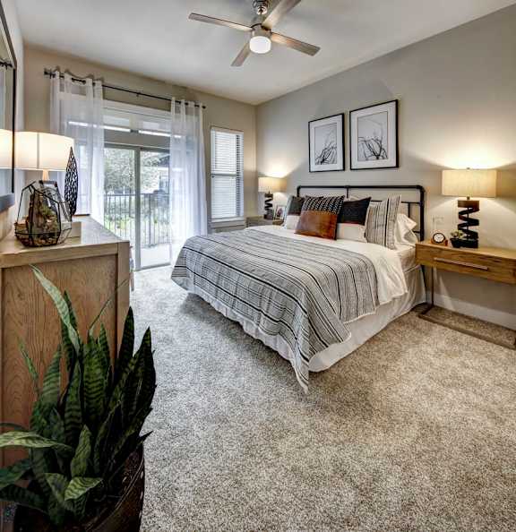 A bedroom with a bed, nightstands, and a ceiling fan at Arise Riverside Apartments, Austin, Texas