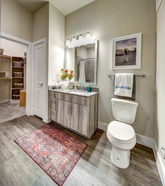 A bathroom with a rug on the floor and a toilet next to a sink at Arise Riverside Apartments, Austin, TX