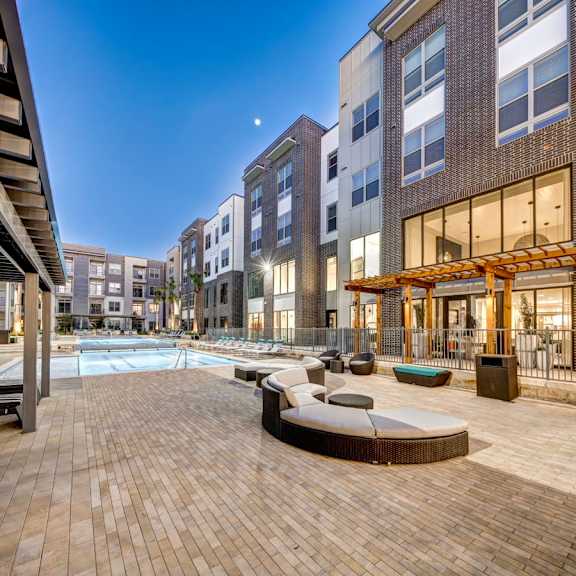A modern outdoor pool area with a wooden deck and lounge chairs at Arise Riverside Apartments, Austin