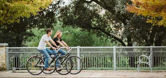 A man and a woman are riding a bicycle together at Arise Riverside Apartments, Austin, TX