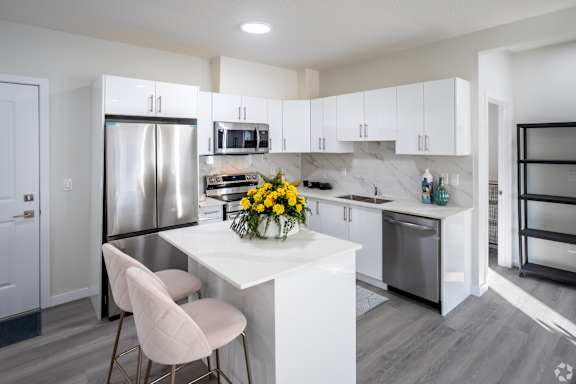 A modern kitchen with a white island and a refrigerator.at Hills on 36, Edmonton, AB T6X 3K2
