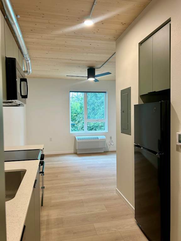 A black refrigerator is in a kitchen with wood floors and a window.