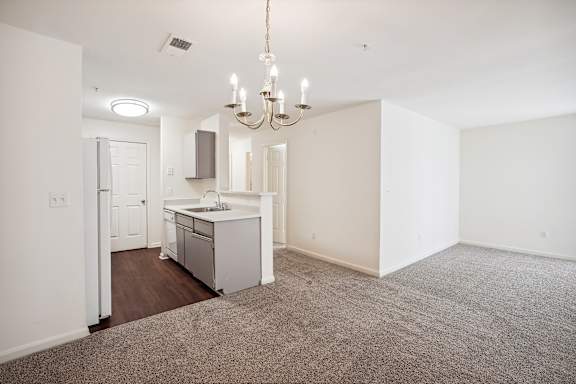 A kitchen with a sink and a refrigerator is in the middle of a room with a carpet on the floor.