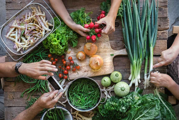 A group of people are preparing food with vegetables on a wooden table.