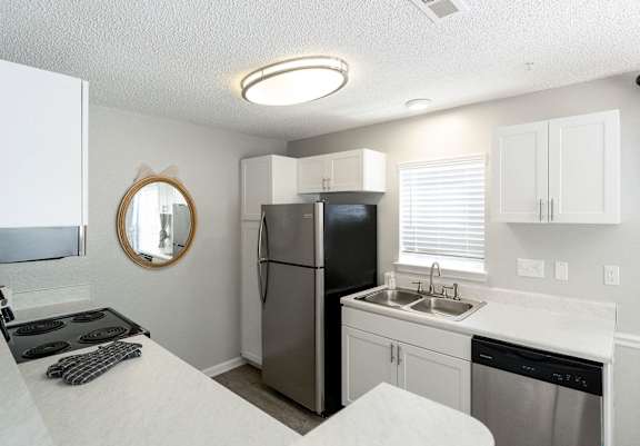 A kitchen with a black fridge, white countertops, and a round mirror on the wall.