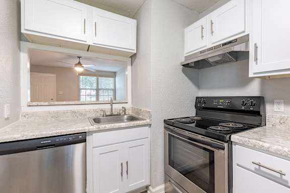 A kitchen with a stove, sink, and cabinets.