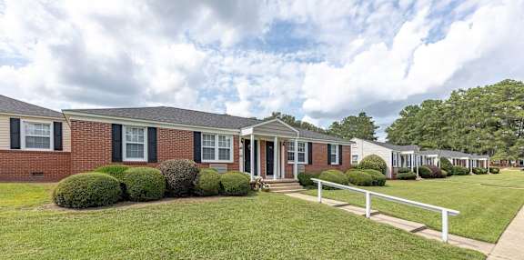 A row of houses with green lawns and white fences.
