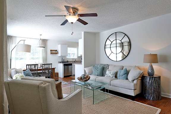 A living room with a beige couch, a glass coffee table, and a ceiling fan.