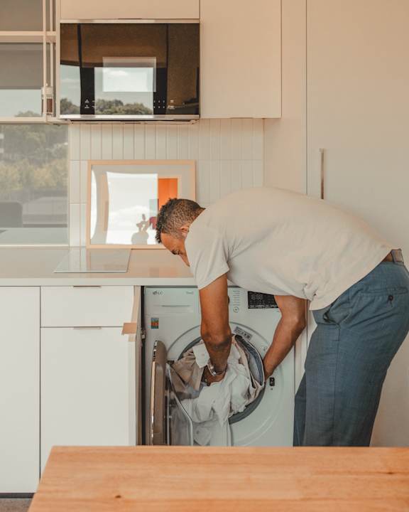 a man is loading a washer into a washing machine in a kitchen at Scout Living, powered by Placemakr Apartments, Atlanta, GA, 30308