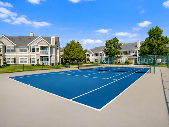 A tennis court is surrounded by apartment buildings.