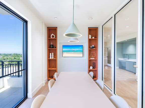 A modern room with a long white table and a television displaying a beach scene.