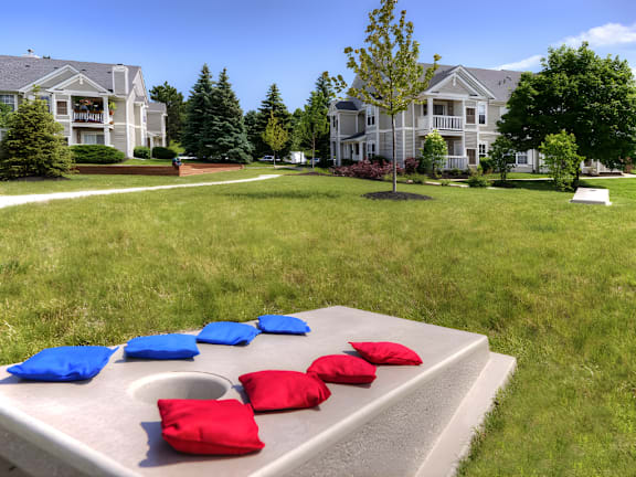 A concrete bench with red and blue cushions in front of a grassy area with houses in the background.