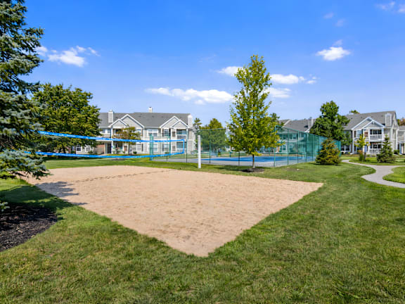A sandy area in front of a building with a tennis court behind it.