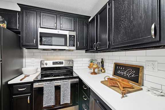 a kitchen with black cabinets and white appliances and a sign that reads stay awhile
