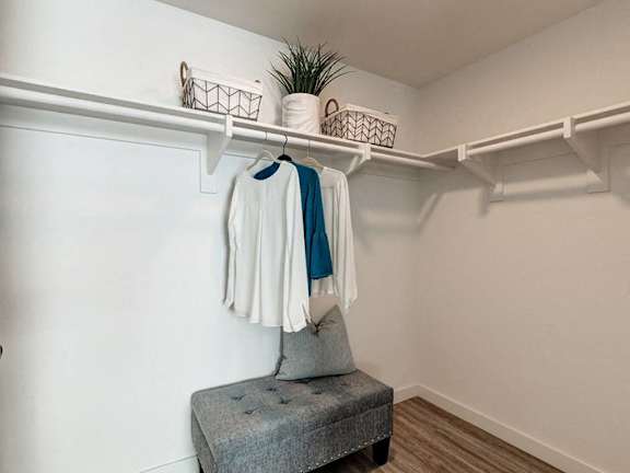 A white chair with a grey cushion is in front of a white wall with a coat hanging on a rail.