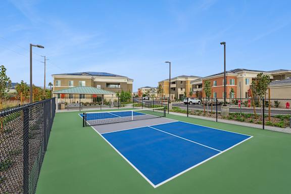 Pickleball court at the Park, surrounded by serene park-like landscaping and benches, and a peaceful pond.