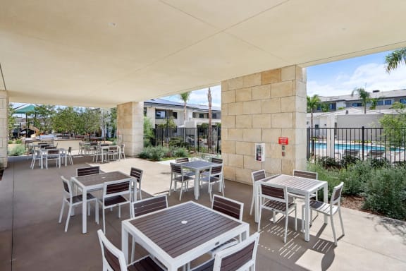 a patio with tables and chairs and a pool at The Max on Jefferson Apartments, Murrieta, CA