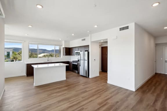 an open kitchen and living room with white walls and wood floors at The Max on Jefferson Apartments, Murrieta