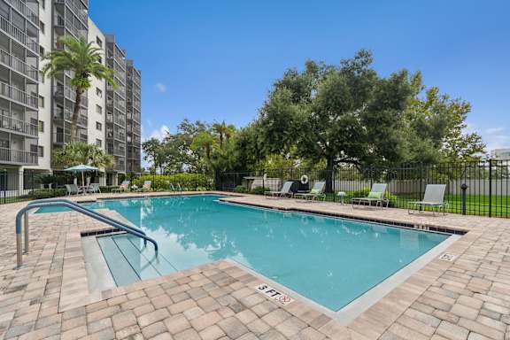 A swimming pool surrounded by a brick patio and lounge chairs at Hampton Apartments, Clearwater