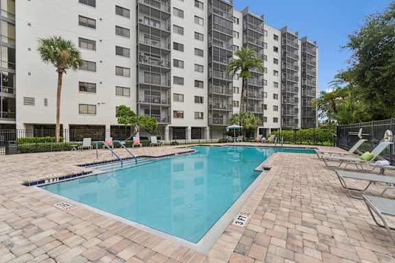 A swimming pool in front of a tall building with palm trees at Hampton Apartments, Clearwater, Florida