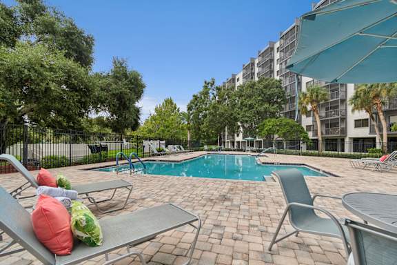 A pool surrounded by chairs and trees with a building in the background at Hampton Apartments, Clearwater, FL