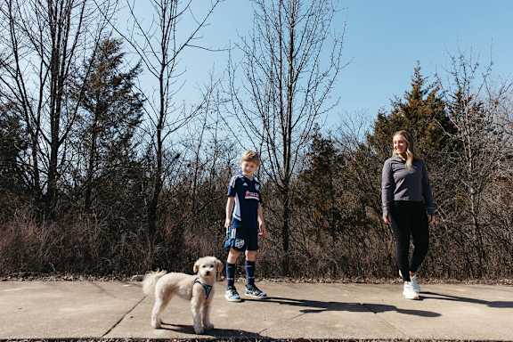 a woman and a boy walking a dog on a sidewalk at The Residences at Tesson Ridge, Saint Louis