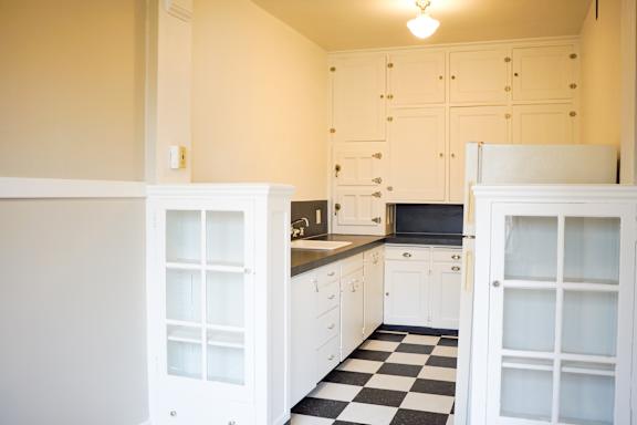 A kitchen with white cabinets and a black and white checkered floor.