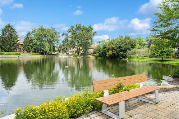 A wooden bench sits on a brick platform next to a lake.