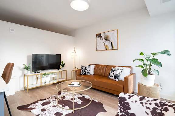 A living room with a brown couch, a glass coffee table, and a TV on a stand.