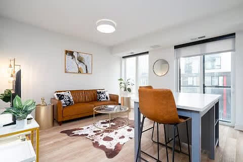 A living room with a brown couch, a white desk, and a rug.