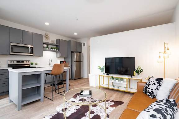 A modern kitchen with a grey island and a brown leather couch.
