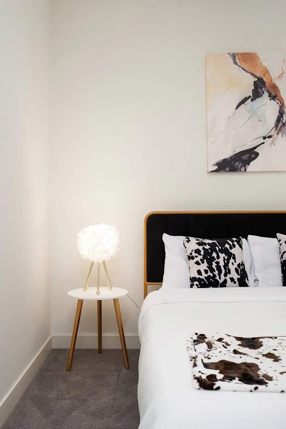 A bedroom with a bed, pillows, a floor lamp, and a painting on the wall.