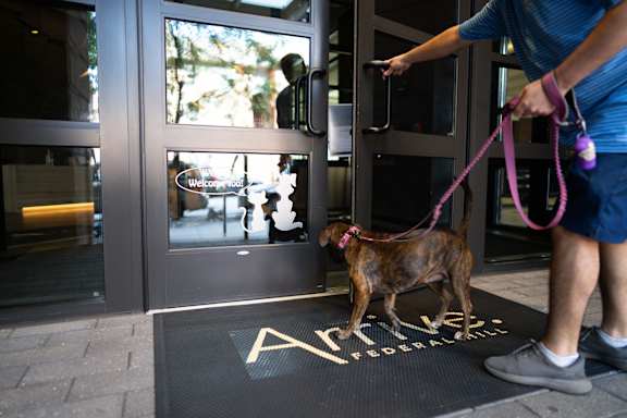 A man is holding a dog on a leash at the entrance of a building.