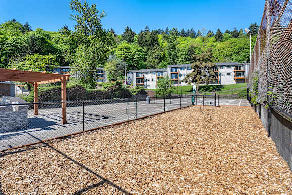 A playground with a brown surface and a fence surrounding it.