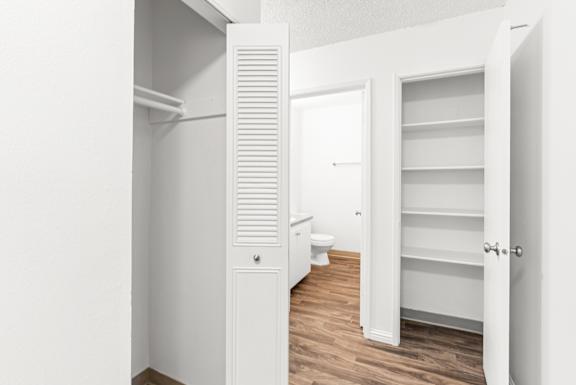 A white bathroom with a toilet and a white closet with shelves.