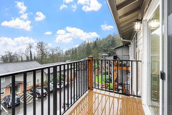 A balcony with a black railing and a view of a parking lot and trees.