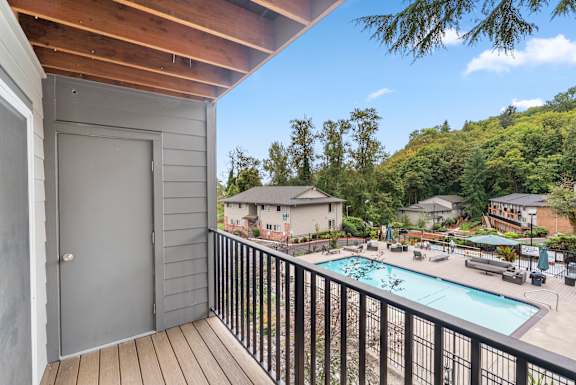 A balcony with a pool and a view of a house and trees.