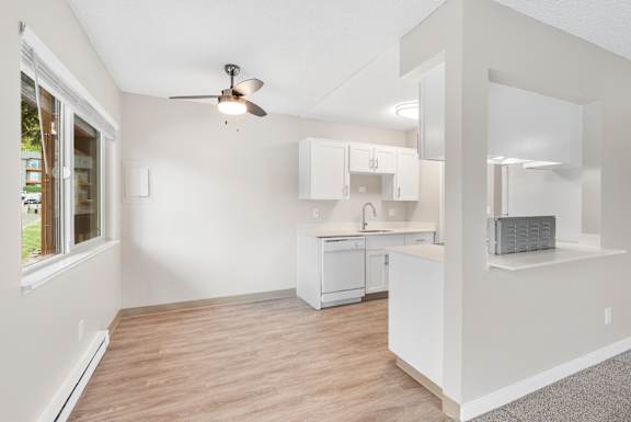 A white kitchen with a ceiling fan and wooden flooring.