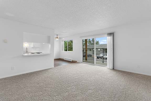 A spacious living room with a carpeted floor and a sliding glass door leading to a balcony.